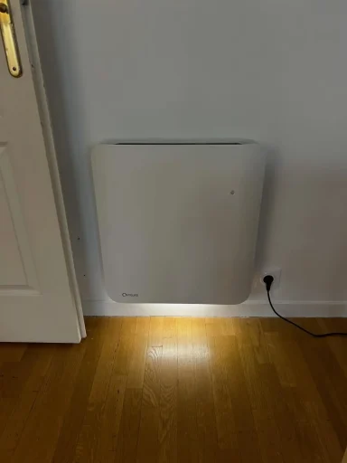 Radiateur électrique moderne blanc fixé au mur, diffusant un éclairage d'ambiance chaud vers le sol en parquet.
