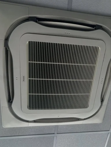 Climatiseur de type cassette encastré au plafond, avec sa grille de ventilation visible.