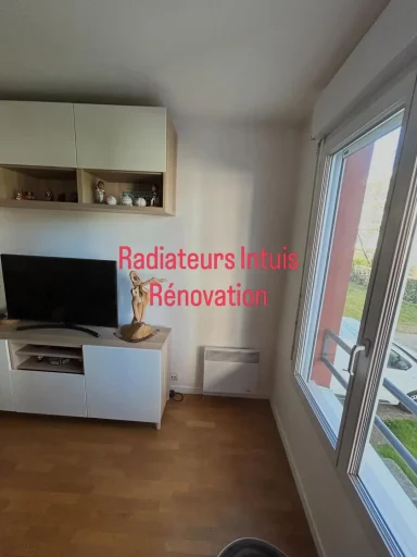 Radiateur électrique blanc installé au mur sous une fenêtre dans un salon à Antony (92), avec la mention "Radiateurs Intuis Rénovation".